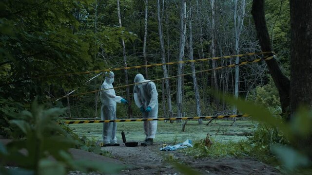 Criminalists working with proofs at crime scene, territory closed with signal tape. Evidence from accident, murder. Investigating proof for forensic examination. Detective workers, medical examiners.