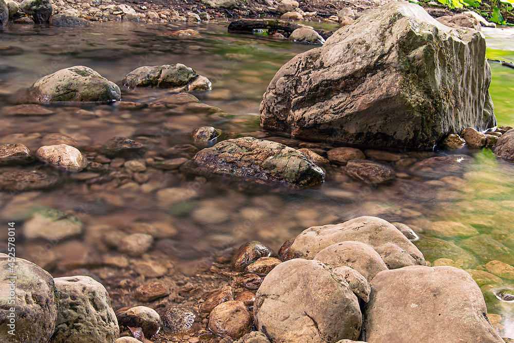 Sticker Closeup view of stones and rocks of various sizes in the water in the forest on a sunny day