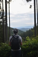 man hiker stands on the edge of the forest and looks into the valley