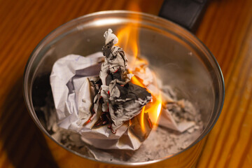 Documents in flames on small silver pot. Official documents destruction, past memories ritual removal, promise commitment, burning evidence concepts