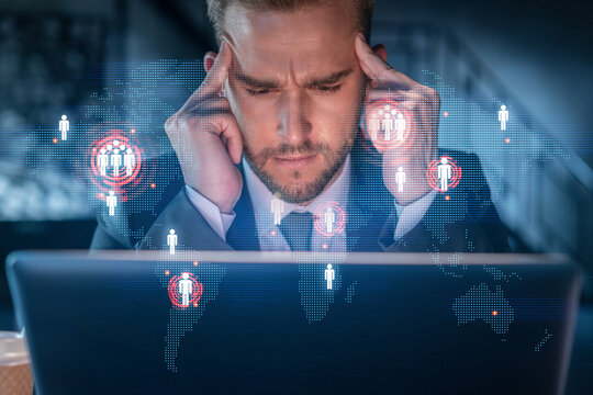 Handsome businessman in suit at workplace working with laptop to hire new employees for international business consulting. HR, social media hologram icons over office background