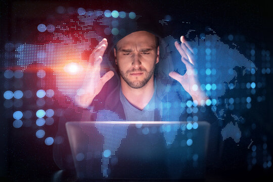 Handsome businessman in hoodie at workplace working with laptop to hire new employees for international business consulting. HR, social media hologram icons over office background