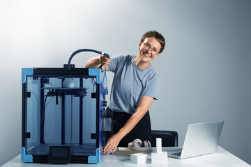 Caucasian beautiful lady in the glasses smiling and adjusting 3d printing machine in her office. New technology for small businesses concept. Computer, prototypes on the table. Tech ambient jpg photo