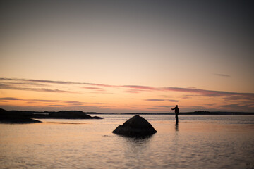 A lone fisherman fishing in shallow waters at night.