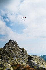 Paraglider silhouette flying over mountains in beautiful warm summer day. Active wallpapers full of freedom. Paraglider flying over a scenic mountainous landscape.