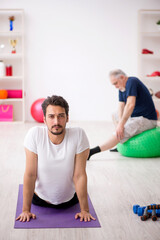 Young male instructor and old man doing sport exercises