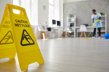 Close up plastic caution sign with figure that slips and falls warning us of wet slippery office...