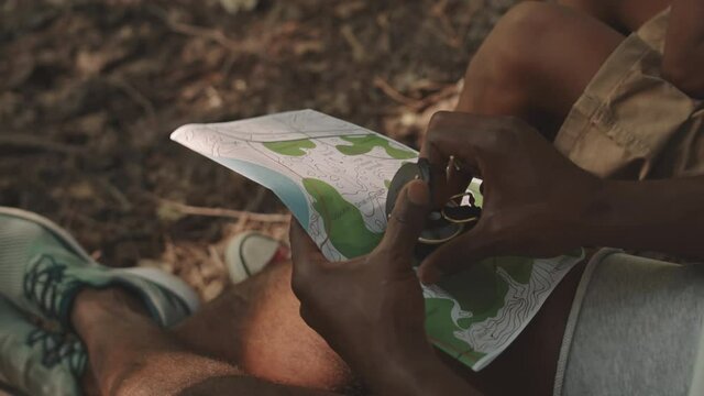 Close-up of unrecognizable African American man using map and compass for navigating in forest during camping trip