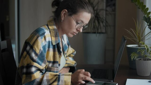 Close-up of brunette woman, in round eyeglasses working at her desk in a home office. Millennial young woman works and use her smartphone. A Girl Is Concentrated Browsing Smartphone
