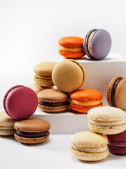 Stack of assortment colorful French Macarons, sweet meringue-base cookies with delicious cream filling, on geometric pedestal display over clean white background. Close Up. Bright light. Warm tone.