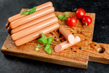 Classic pork sausages on a cutting board with basil and ketchup on a stone background