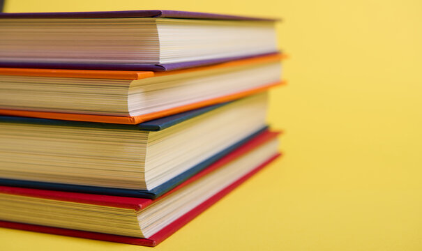 Close-up of stacked multicolored books on yellow surface background with copy space for text. Teacher's Day concept, Knowledge, literature ,reading, erudition