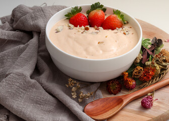 banana, papaya and coconut smoothie accompanied by Strawberries and Brazil nuts, in a white bowl and decorated with dried flowers