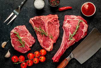 A variety of raw steaks. Ribeye steak, tomahawk, T-bone, on a stone background