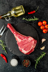 raw Tomahawk steak with spices ingredients on a stone background