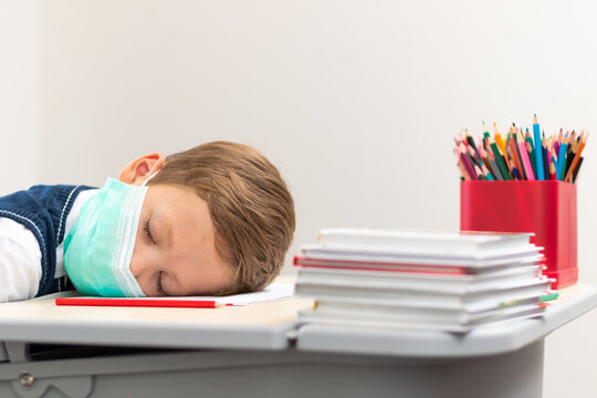 A cute first grader boy in a school uniform at his desk wearing a protective medical mask during the coronavirus pandemic. Selective focus. Close-up. Portrait