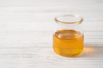 The small honey glass jar on the white wooden table. One portion of honey to serve the dessert.