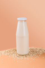 Vegan non dairy alternative milk. Oat milk in a bottle on the oat flake on pastel peach terracotta color background, above, copy space