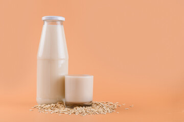 Trendy Vegan non dairy alternative milk. Oat milk in bottle and in a glass on the oat flake on pastel peach terracotta color background, copy space
