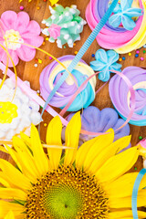 Assorted colorful meringues and sunflowers on a wooden background