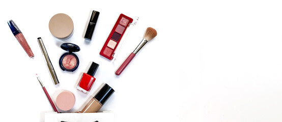 Beauty concept. Makeup products shadows, highlighter, blush, brushes, powder, glitter, mascara, gloss, lipstick, pencil on white background under white gift bag