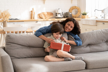 Birthday gift for small kid: joyful caring mom greeting child presenting little preschool boy...
