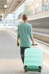 Back image of a woman going to catch her train. Vertical photo. Turquoise blazer and suitcase. Business women