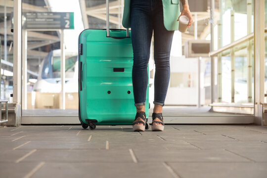 Detail photo. Girl standing with rolling suitcase and glass of coffee. Business woman. Enterprising women. Travel and work.