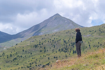 young woman in mountain clothes, contemplating a large Pyrenean mountain in the background, on a...
