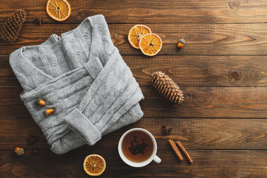 Wooden table with knitted sweater, tea cup, acorns, dry oranges, cinnamon stick. Autumn fall, hygge feminine desk. Flat lay, top view.