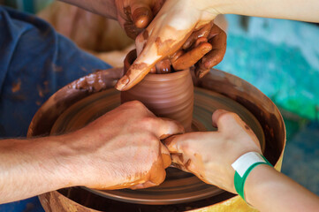 A potter makes a clay pot on a potter's wheel and conducts a master class. Hands of the master and the child close up while studying