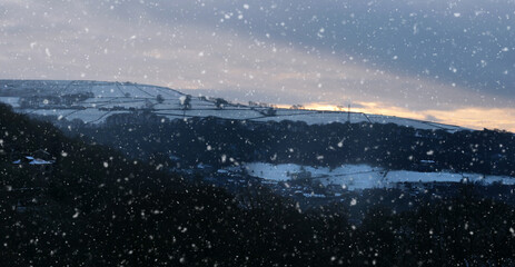 panoramic view of a glowing orange sunset in a cloudy twilight winter sky with falling snow in calderdale west yorkshire