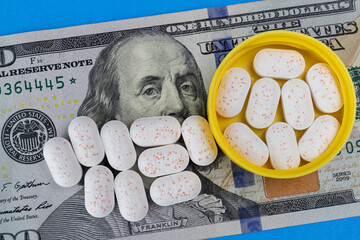 Hydrocodone tablets in a yellow cap against a hundred dollar bill. Opiate addiction costs the U.S....
