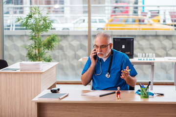 Old male doctor working in the clinic in telemedicine concept