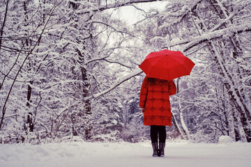 A happy woman stands with a red umbrella in her hands, a winter park with snow-covered trees