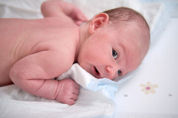 A baby aged one month is lying in a crib on his stomach. A Caucasian boy child in a home white bedroom