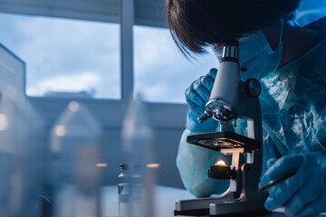 Asian medical scientist using microscope analyzing covid samples inside laboratory hospital - Focus...