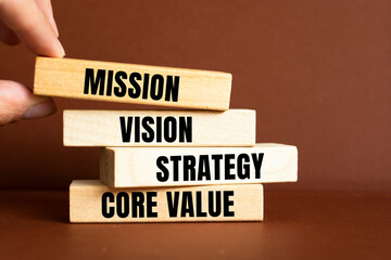 Businessman hand holding wooden building blocks with MISSION, VISION, CORE VALUE and STRATEGY word. Business concepts