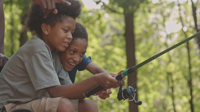 Slowmo shot of cheerful African American boys fishing together outdoors in forest on summer day