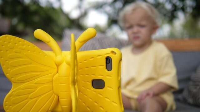 Back of yellow child proof butterfly tablet case. Blurred white toddler in the background watching it.