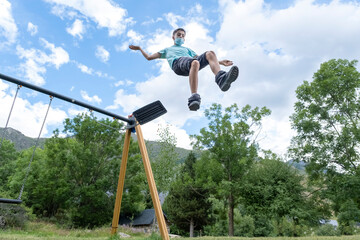 young guy wearing a sanitary mask makes a huge jump from a swing on a playground, leaping into the...