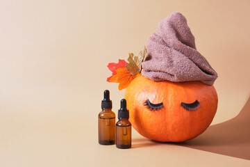 mock up cosmetic containers with pipettes and pumpkin with towel and eyelashes on beige background, skin care in autumn