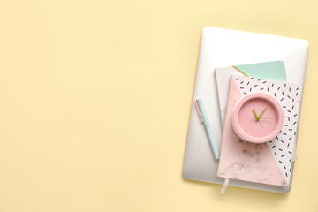 Alarm clock with office supplies and laptop on color background