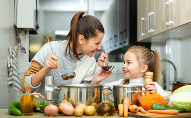 Happy young mother and small daughter tasting vegetable soup together