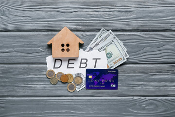 Word DEBT with money and house figure on dark wooden background