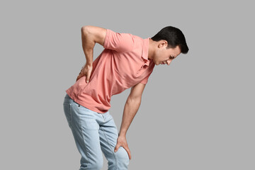 Young man suffering from back pain on grey background