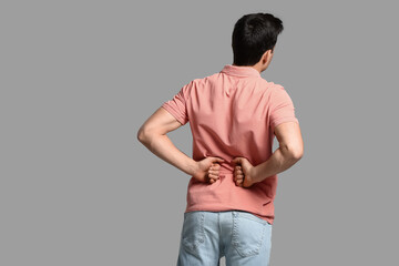 Young man suffering from back pain on grey background