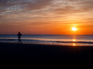 Fototapeta na wymiar silhouette of a man running on the beach during sunrise