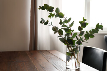 Vase with eucalyptus branches on table in room