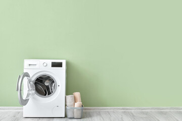 Modern washing machine with clean towels near color wall